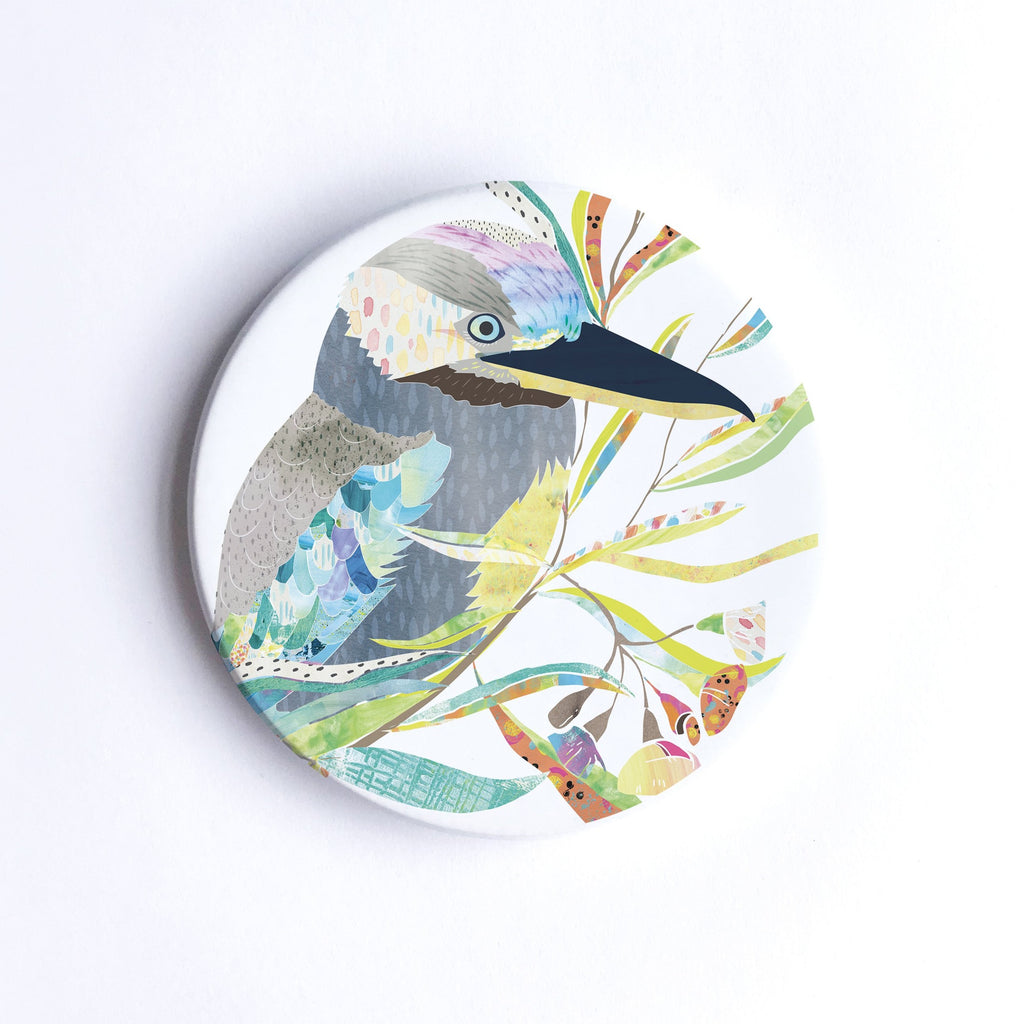        Round, hand printed ceramic coaster with illustration of a grey, blue- winged           kookaburra bird on a branch with colourful leaves.           