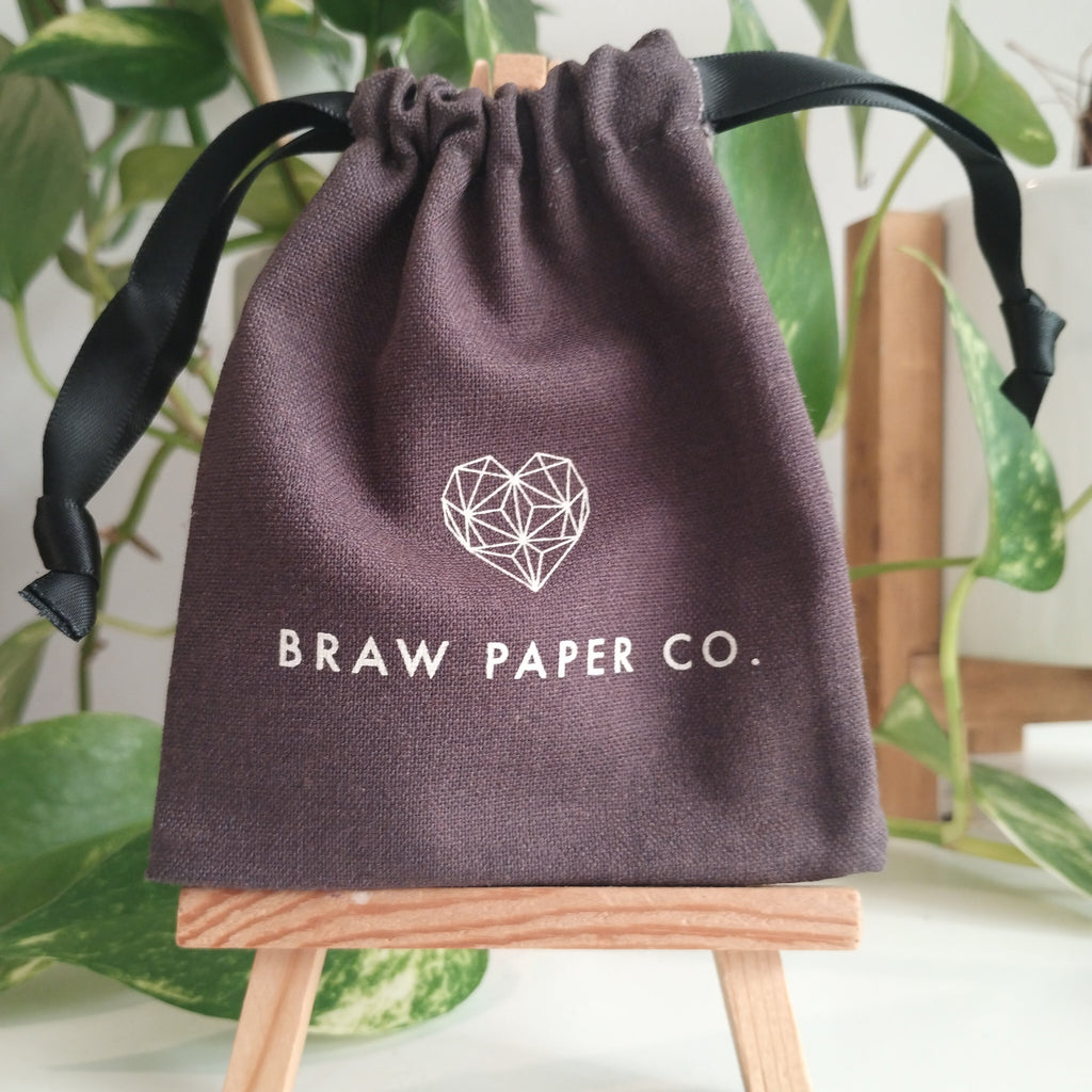 Dark grey linen pouch with black ribbondrawstrings with 'Braw Paper Co.' logo printed onto it. background
