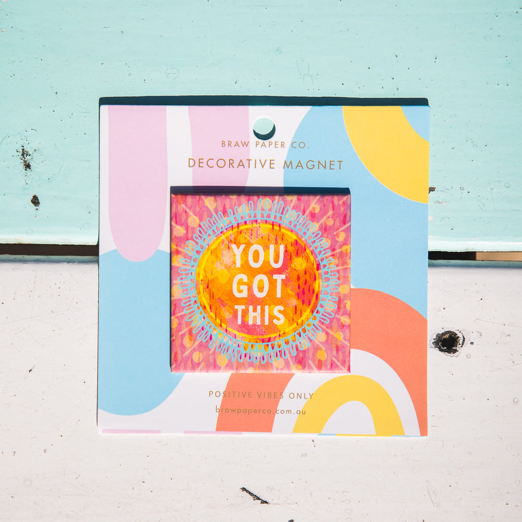 Decorative magnet with 'You Got This' text on a colourful background, attached to a light blue wall.