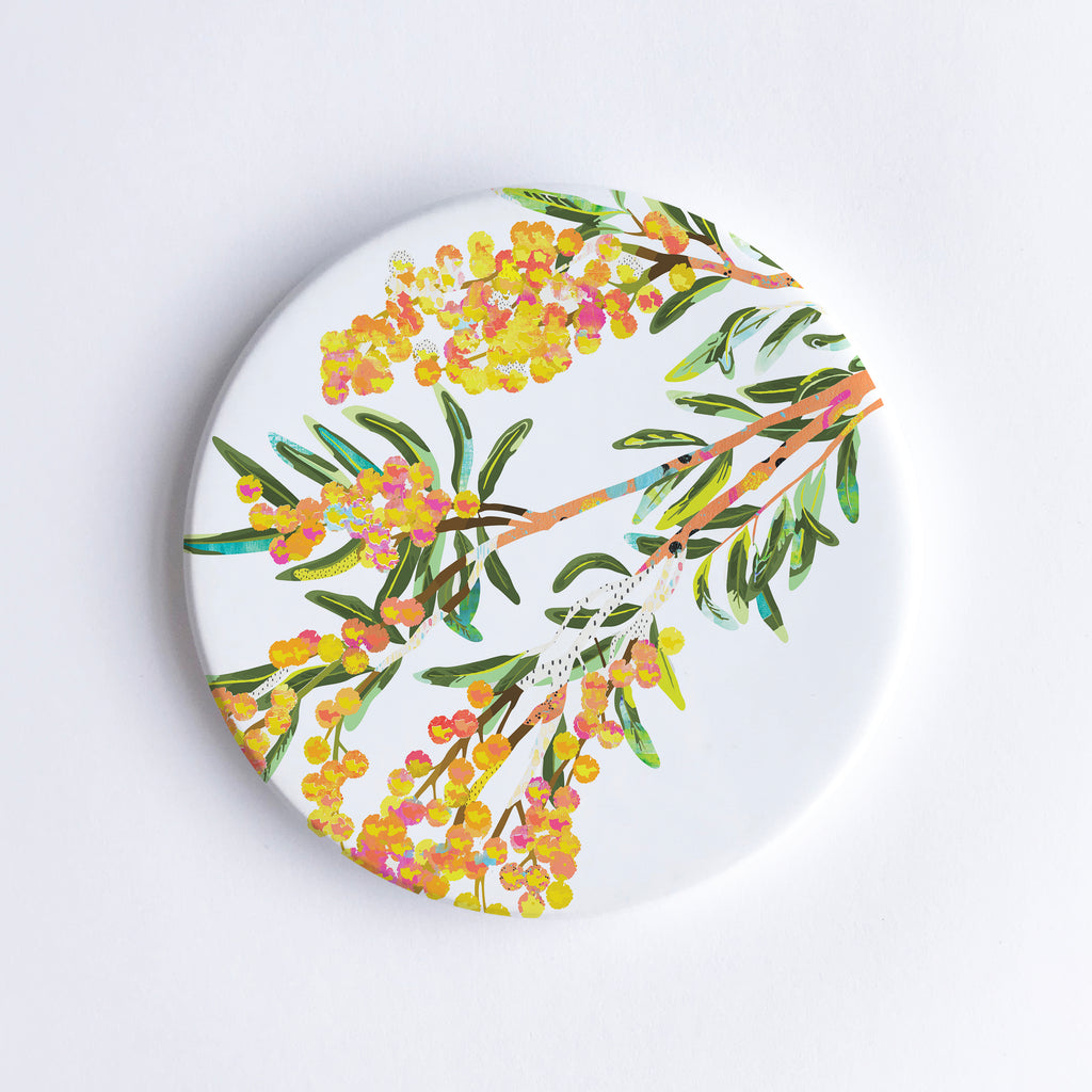 A ceramic coaster with a hand-printed acacia or wattle design, predominantly featuring yellow and green colours, with a white background.