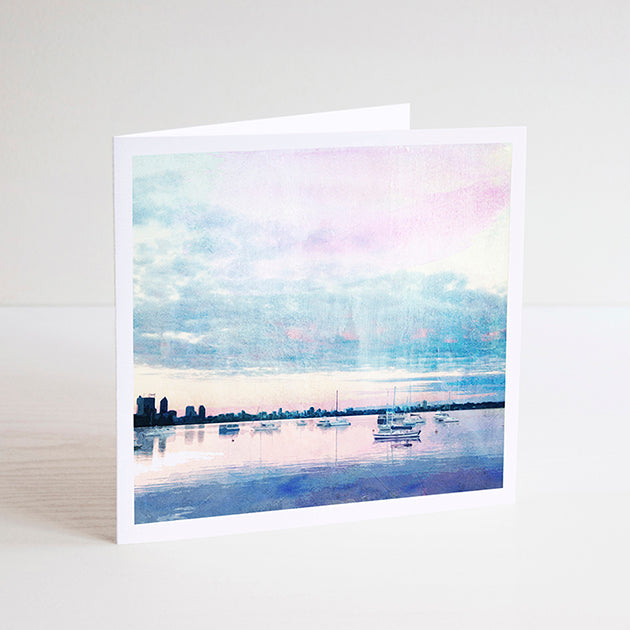 Square notecard with illustration of Matilda Bay at dusk, sailing boats on Swan River and Perth city skyline in the background. 
