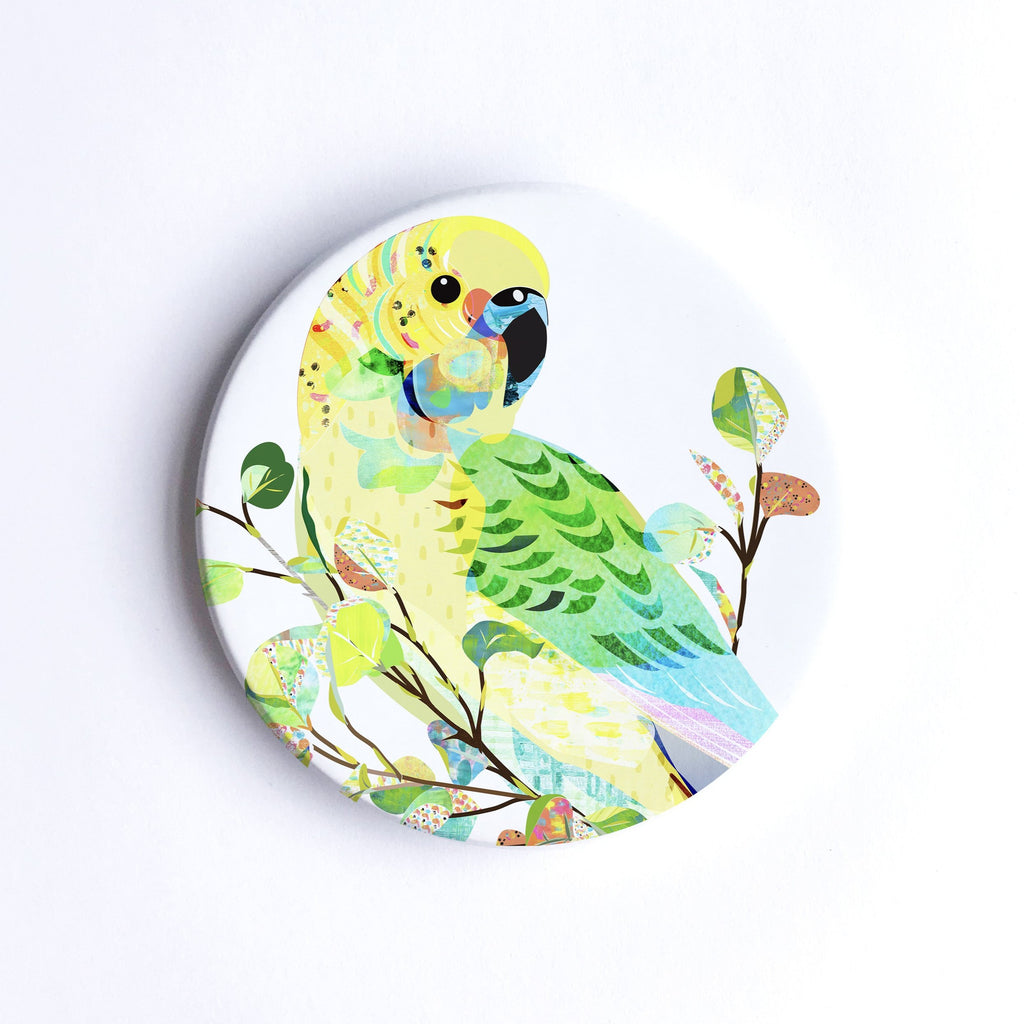 Round, hand printed ceramic coaster with illustration of a green and yellow Budgerigar bird on a branch with colourful leaves.