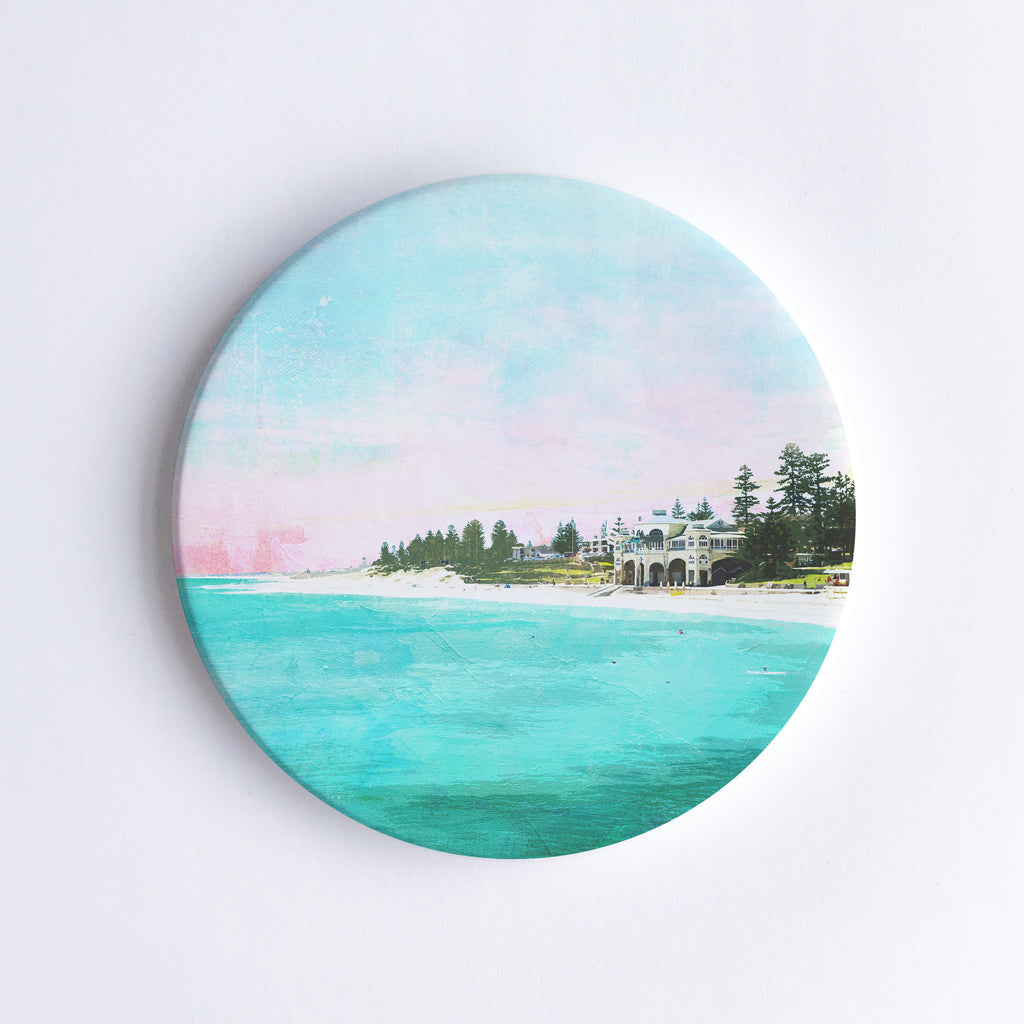 Round, hand printed ceramic coaster with illustration of Cottesloe Beach and the Indiana teahouse surrounded by trees during sunset.