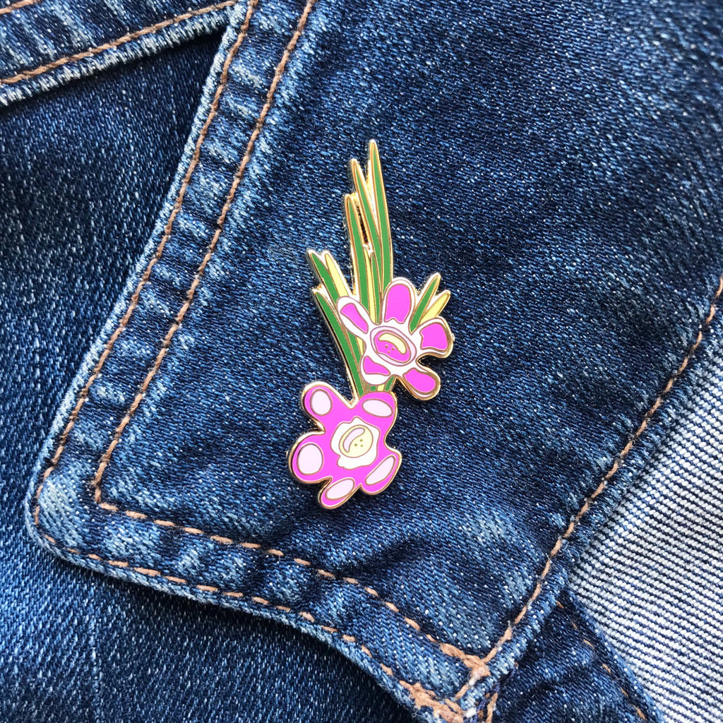        Enamel pin with a pink, purple, yellow and green Geraldton wax flower illustration.