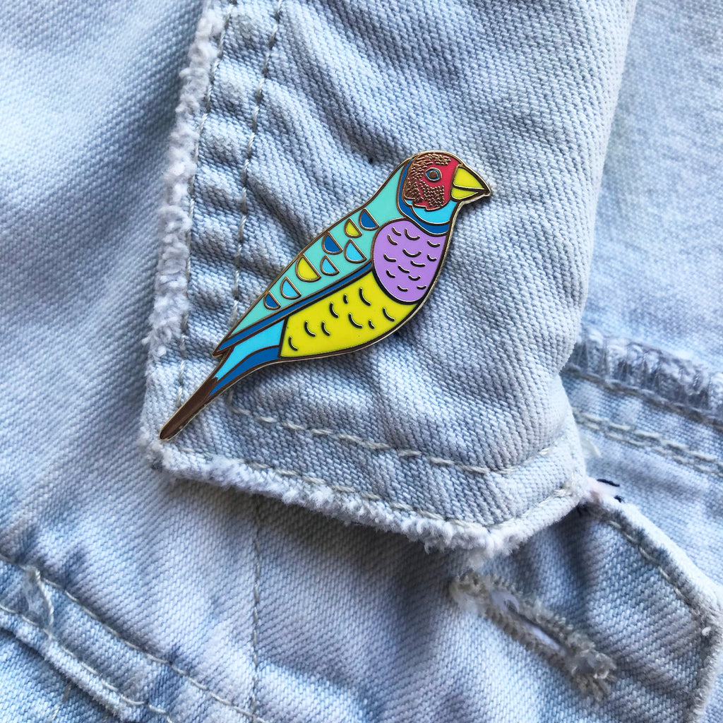 Enamel pin with purple, yellow, blue and red Gouldian Finch illustration.
