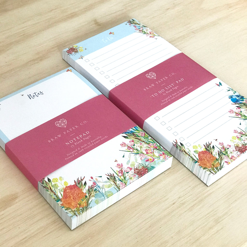 Blank A6 notepad with blue wren bird, butterflies and colourful Australian native flora illustration next to a lined to do list notepad with the same design.