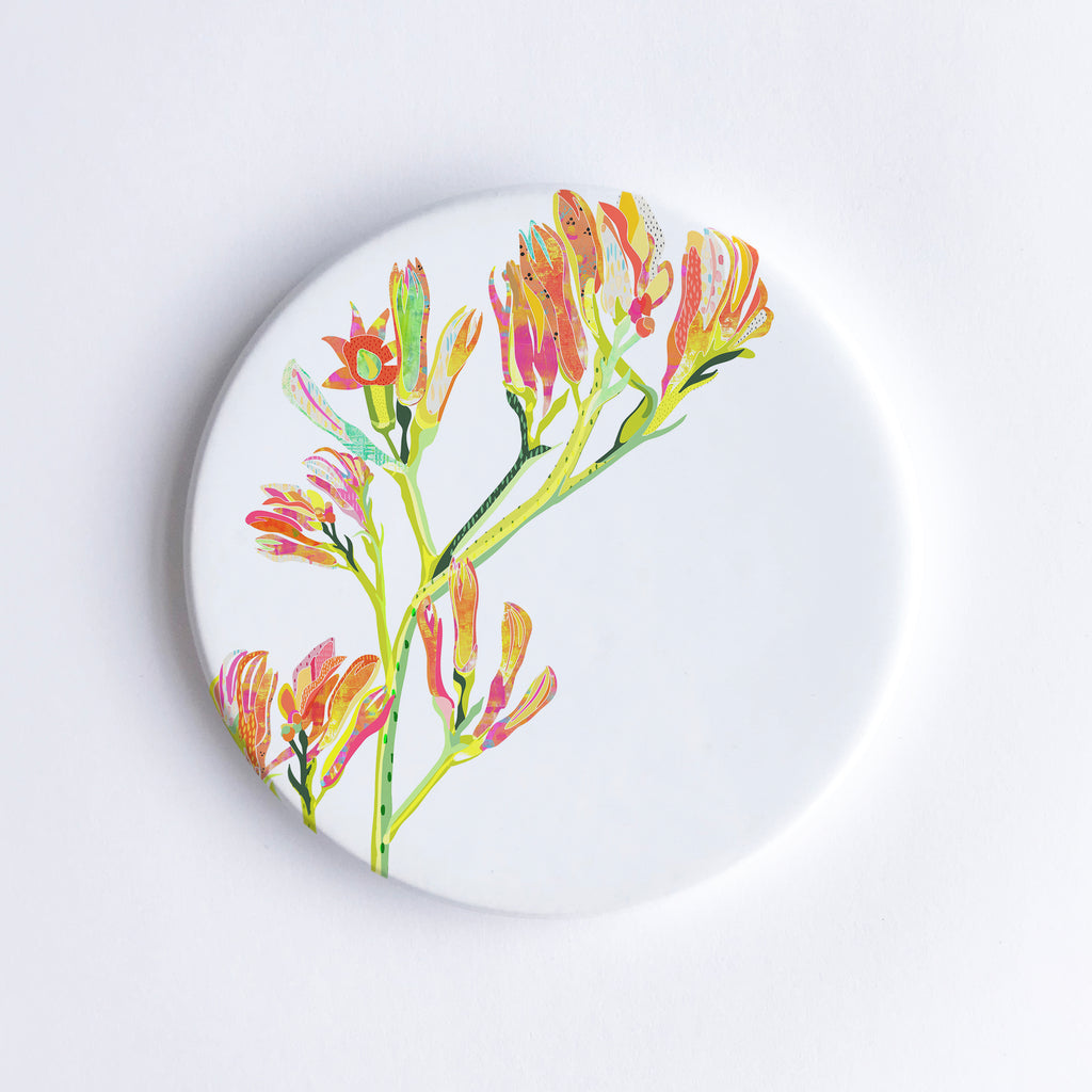 Round, hand printed ceramic coaster with illustration of red, yellow, orange and pink kangaroo paw flowers illustration.