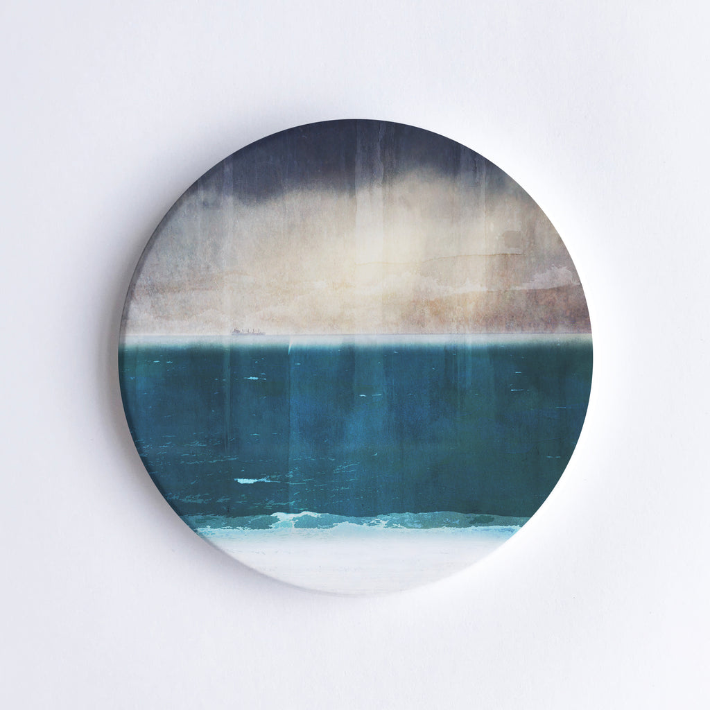 Round, hand printed ceramic coaster with illustration of Port Beach in Western Australia with dark, moody sky before a storm.