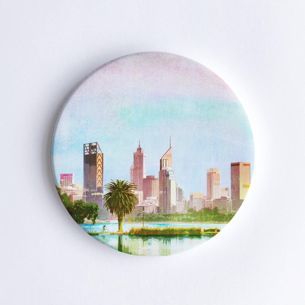 Round, hand printed ceramic coaster with illustration of Perth city skyline behind a palm tree.
