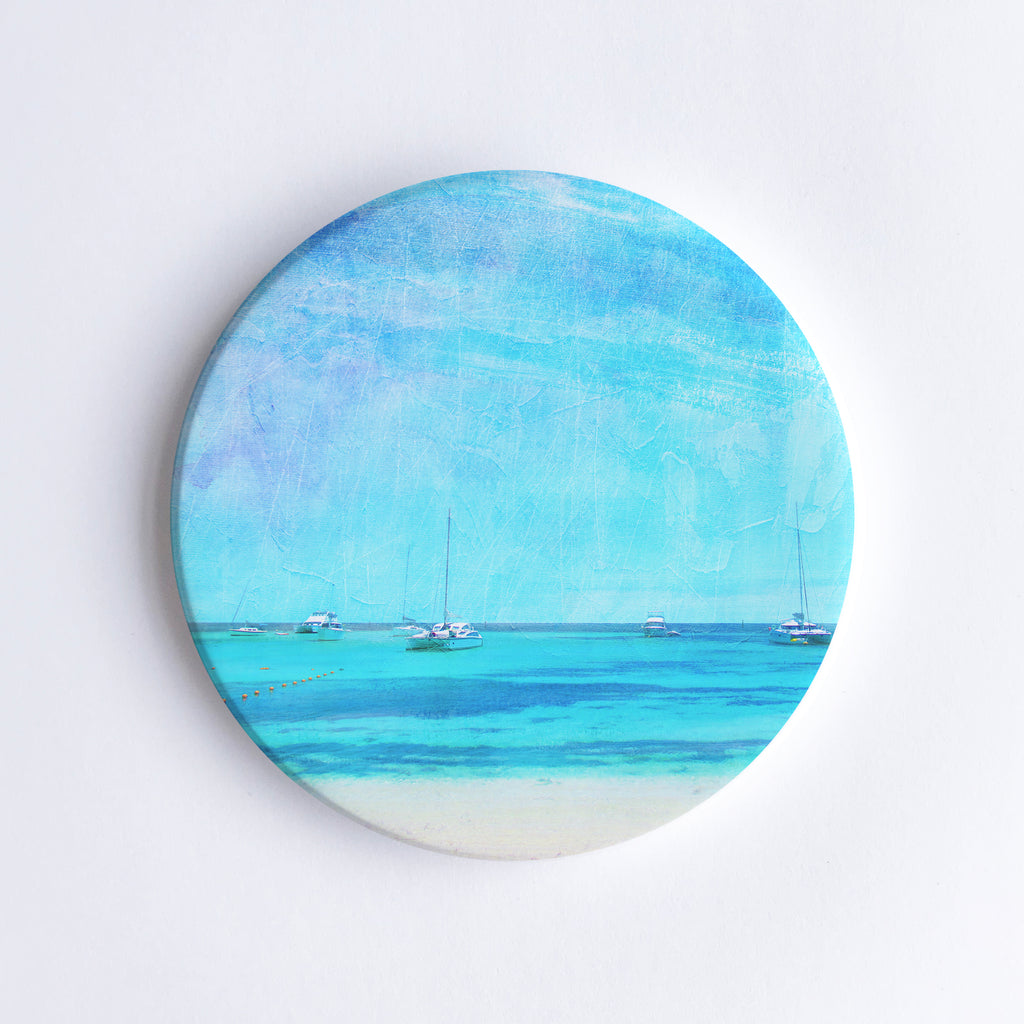 Round, hand printed ceramic coaster with illustration of Rottnest Island with sailing boats in the turquoise sea.