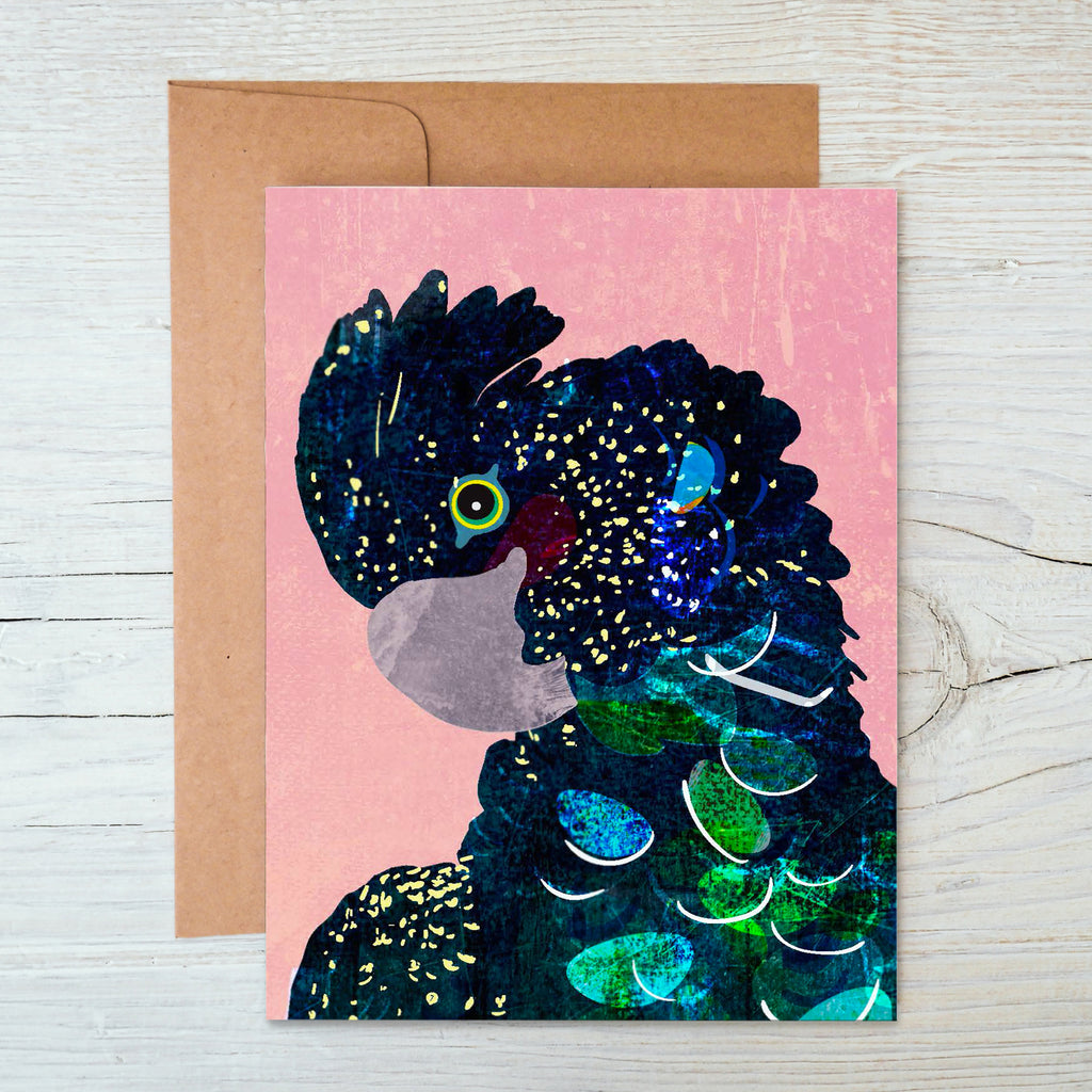 A notecard featuring a mixed media illustration of a red-tailed black cockatoo with a pink background, accompanied by a brown kraft envelope.