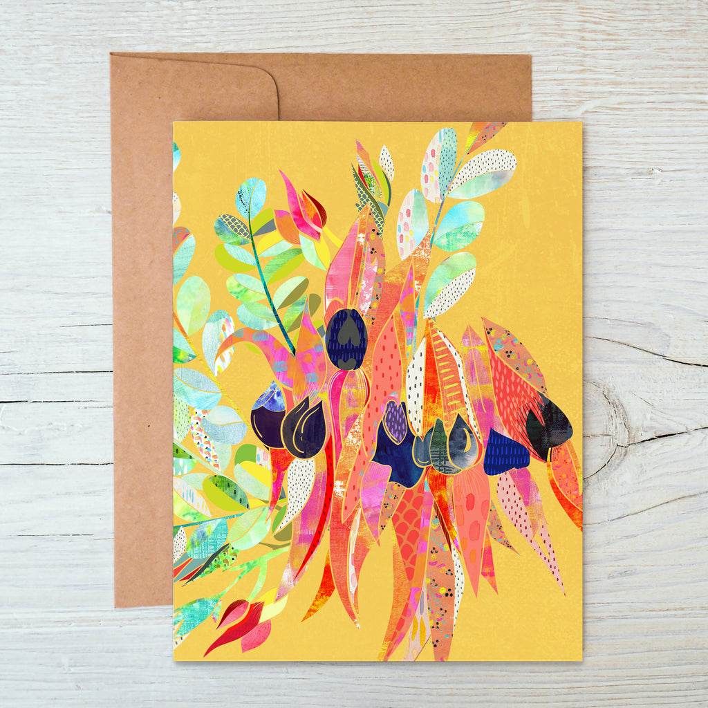 A colorful A6 notecard featuring a floral design with a Sturt Desert Pea motif, accompanied by a brown kraft envelope, displayed against a wooden background.