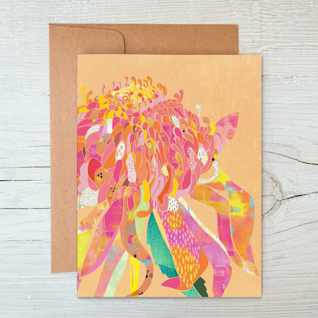 A pink notecard featuring an illustration of a waratah flower, with a brown kraft envelope, placed on a wooden surface.