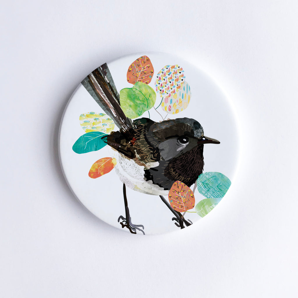 A ceramic coaster with a hand printed image of a Willie Wagtail bird surrounded by colourful abstract designs on a white background.
